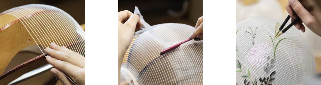 製作中的淺色燈籠，燈籠結構由木製骨架支撐，覆蓋著細緻的白色條紋紋理，上面裝飾著粉色花朵和綠色植物圖案。