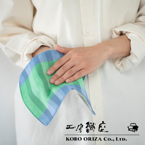 一條長方形手帕，採用藍色和綠色格紋圖案，材質為棉。手帕由人手持握，展示其柔軟的質地和精緻的編織。