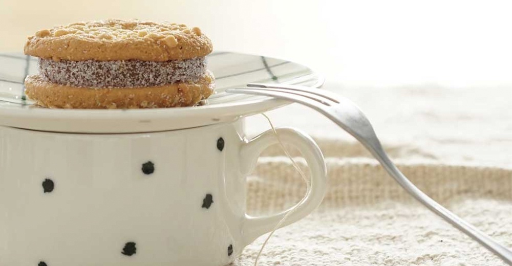 一個點心盤，上面放著夾心餅乾，盤子下方是一個帶有黑色圓點圖案的白色陶瓷杯，旁邊放著一把叉子。