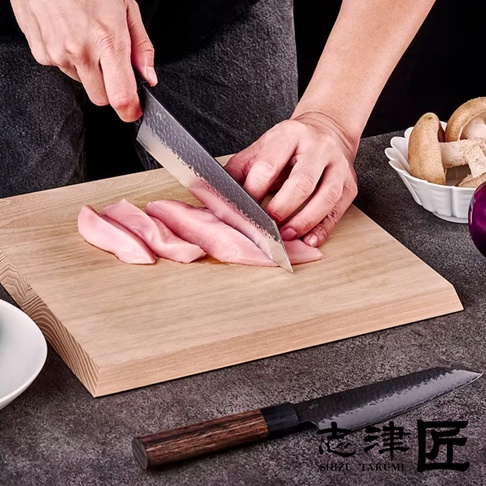 玄 / Bunka 文化刀19cm，刀身為鍛造紋理的銀色鋼材，配有深棕色木質手柄。刀正用於切割木質砧板上的粉色肉類，旁邊另有一把同款刀具，以及碗裝的香菇和紫色洋蔥。