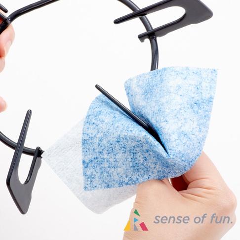 一隻手拿著黑色瓦斯爐架，另一隻手使用一片藍白相間的去汙清潔巾擦拭。清潔巾材質纖維狀，帶有細緻的藍色斑點。