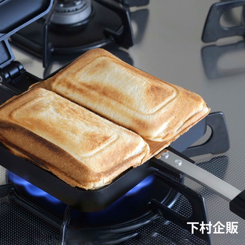 直火式壓邊吐司烤盤，黑色烤盤內有兩塊金黃色、壓有格紋的吐司，烤盤置於瓦斯爐上，底部有藍色火焰。
