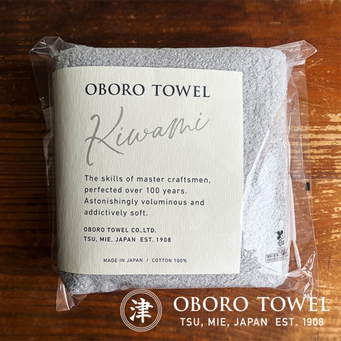 一款淺灰色細纖浴巾，材質標示為純棉，包裝上有「OBORO TOWEL Kiwami」字樣，並註明「MADE IN JAPAN」、「COTTON 100%」。