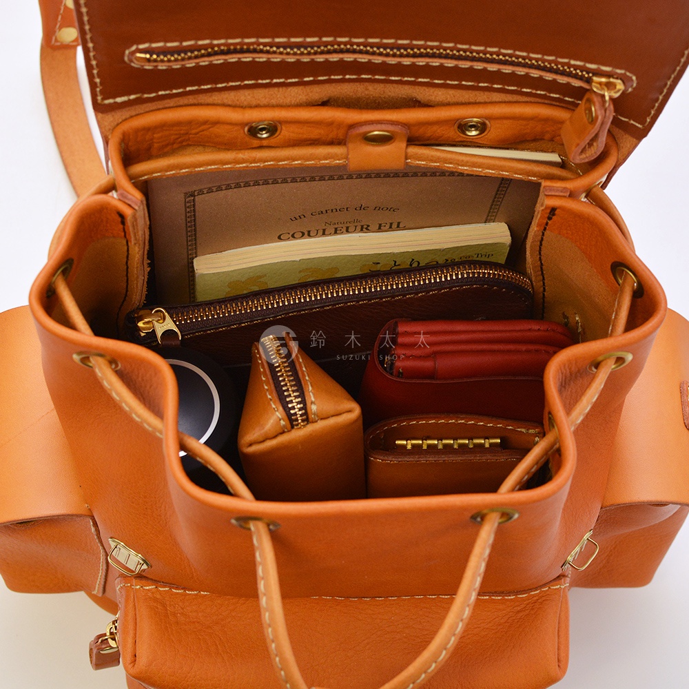 職人手作皮革復古風旅行後背包 R-65，展示內部空間，駝色皮革材質，裝有筆記本、化妝包、錢包及鑰匙包。