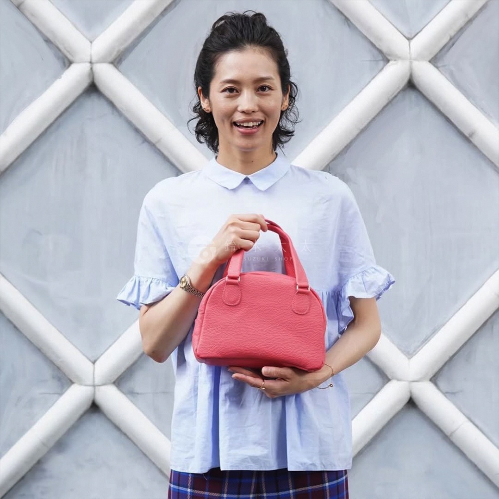 一位女性手持亮粉色皮革半月迷你手提包，包身帶有紋理，配有兩個短提把。