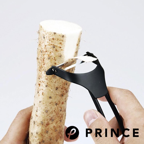 一支黑色削皮器正在削去一根山藥，削皮器採用人體工學設計，握柄為黑色，刀片為金屬材質，展現其高效的削皮功能。