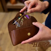 一雙金屬鏡架的玳瑁紋眼鏡，正在被放入一個手工皮革眼鏡收納盒中。收納盒為棕色，帶有金屬按扣。