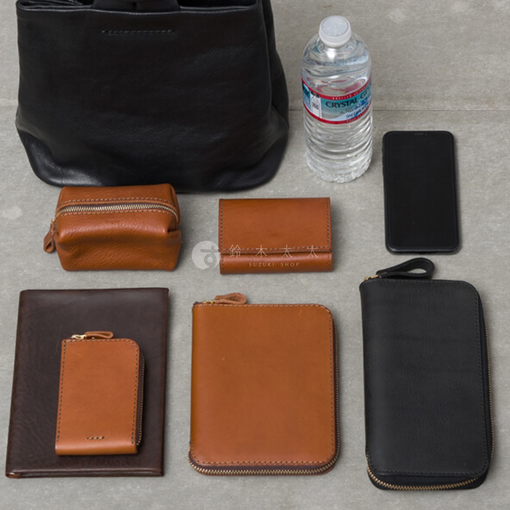 職人手作皮革Organ單柄手提包 G-87，包含一個黑色手提包、一個棕色方形零錢包、一個棕色對摺錢包、一個棕色長夾、一個棕色小皮夾，以及一個黑色長夾。另有瓶裝水與手機。
