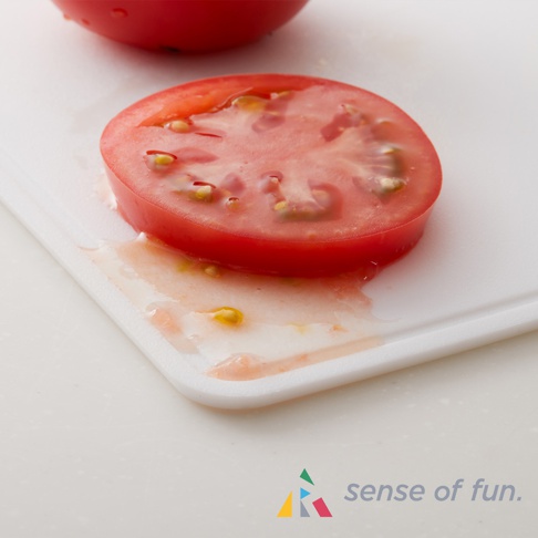 白色矽膠砧板上放著一片切片番茄，番茄汁液滲出。