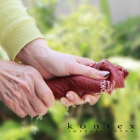 雙手正擰著一塊深紅色的 MOKU 超速乾輕薄吸水小方巾，水珠從布料中滴落。毛巾質地細緻，有明顯的紋理，部分區域可見「MOKU TOWEL IMABARI JAPAN」字樣。