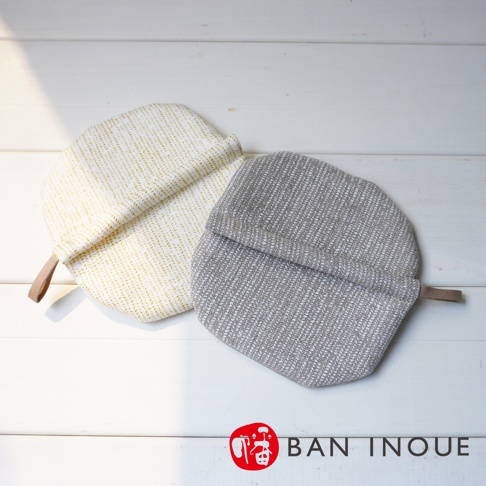 兩件 Tricot 棉麻防燙鍋套，一件為米白色，印有金色細條紋；另一件為淺灰色，織有斜紋。