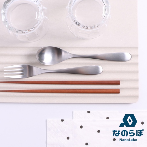 珪藻土置物墊上擺放著兩個透明玻璃杯、一個金屬湯匙、一把金屬叉子，以及兩雙深棕色木質筷子。