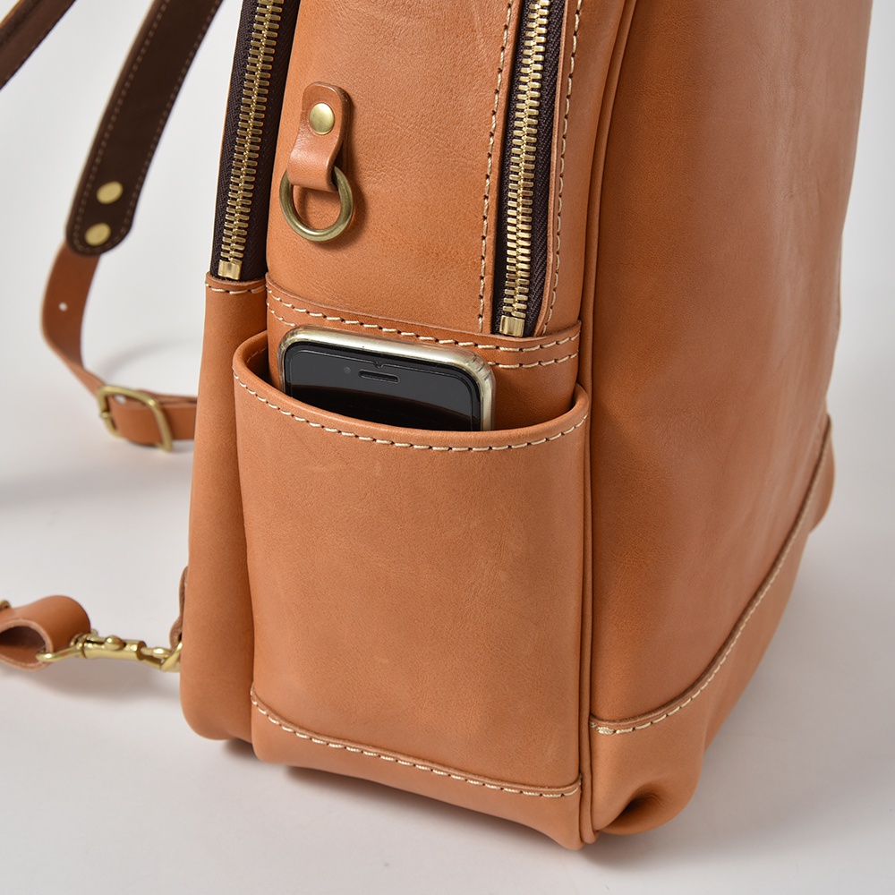 職人手作皮革多功能後背包 R-21，主體為棕色皮革，側邊有一個可放入手機的開放式口袋，並有金屬拉鍊和掛環細節。