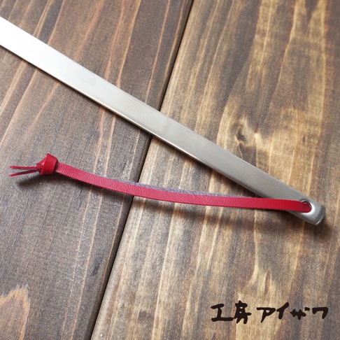 不鏽鋼萬用撈油勺，勺面為銀色不鏽鋼材質，帶有紅色皮革掛繩，掛繩末端為打結設計。