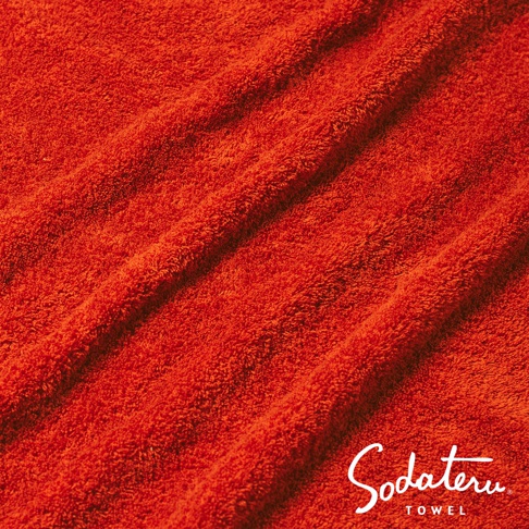 紅色毛巾上的陰影和紋理，右下角有 Sodateru TOWEL 的品牌標誌