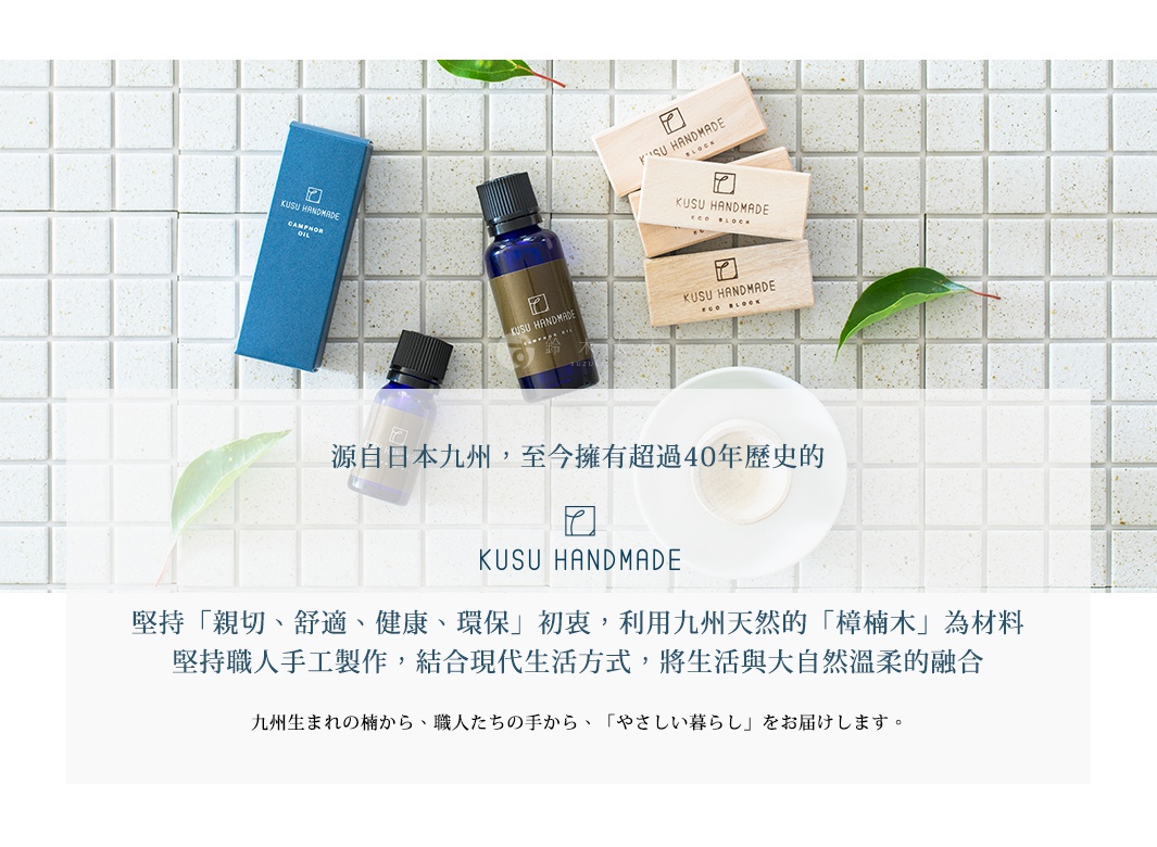 藍色紙盒裝的樟腦油，淺紫色瓶裝的精油，數個寫有「KUSU HANDMADE ECO BLOCK」的淺木色木塊，以及一個白色圓形盤子，背景為白色小方塊瓷磚。
