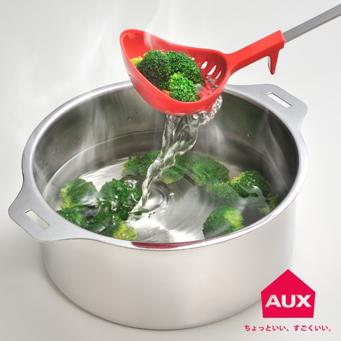 紅色濾水湯匙正從裝有西蘭花的鍋中瀝水，湯匙裝有幾塊煮熟的西蘭花，水從湯匙的孔中流出，滴入銀色金屬鍋中。