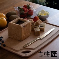 金屬材質的麵包刀，帶有鋸齒狀刀刃，刀柄為金色，置於淺棕色木質砧板上，旁邊是方形吐司、草莓、藍莓、橘子、奇異果及一碗奶油。