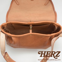 職人手作皮革郵差包，採用天然棕色皮革，包身線條簡潔，內部有置物夾層，搭配金屬扣環與皮革背帶。