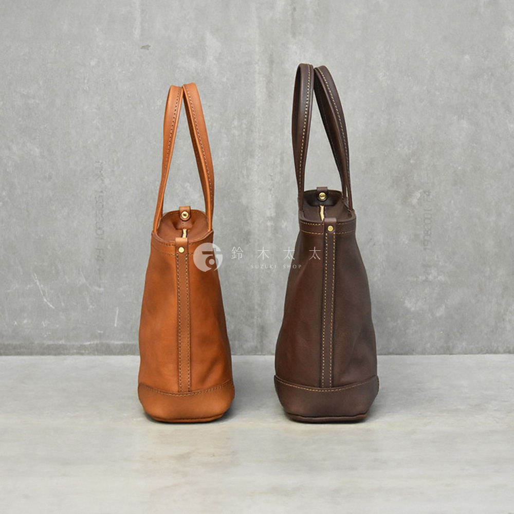 兩款職人手作皮革托特包，一款為淺棕色，另一款為深棕色，皆為側邊視角，展現包款的皮革質感與縫線細節。