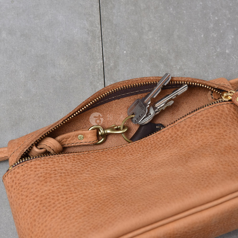 一個打開的棕色皮革斜背包，裡面裝著一把鑰匙，包包的拉鍊是金屬材質。
