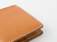 職人手作皮革二折直式短夾，展示淺棕色皮革表面，搭配米白色縫線，材質為真皮。