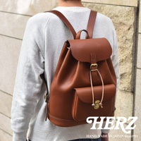 棕色皮革經典後背包，設有翻蓋、抽繩束口、前置口袋及金屬扣環，皮革材質，簡約設計。