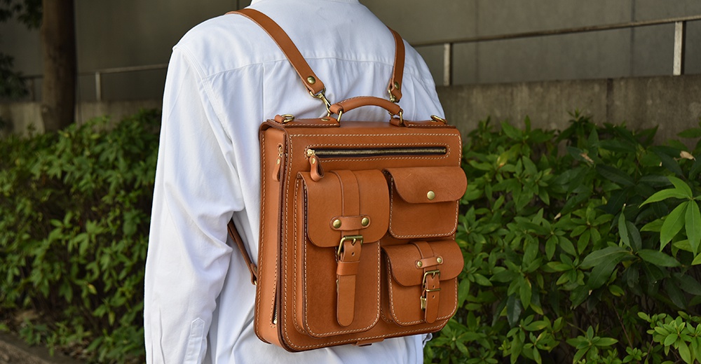 職人手作皮革三口袋三用後背包，採用棕褐色皮革，設有三個翻蓋口袋、一個拉鍊袋及頂部提把，配有可拆卸肩帶。