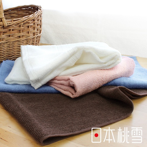 堆疊的居家浴巾，顏色包含深棕色、藍色、粉紅色和白色。浴巾質地柔軟，表面有明顯的織紋。畫面左側有一個編織籃。