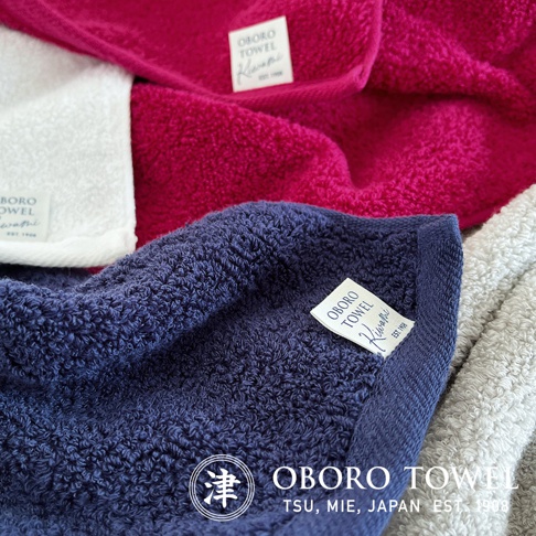 三條細纖浴巾，顏色分別為深藍、桃紅、白色及淺灰色，皆為柔軟毛圈材質，帶有品牌標籤。
