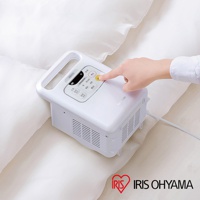 白色IRIS OHYAMA雙筒強力烘被機 FK-W1，置於白色被褥上。機身頂部有黑色控制面板，顯示多種烘乾模式按鈕，一隻手正按下黃色「停止」按鈕。