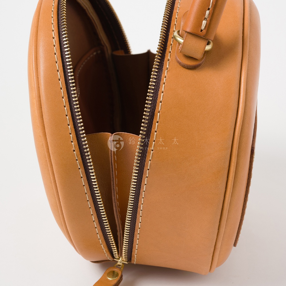 日本HERZ職人手作皮革兩用圓形包Q-13，棕褐色Latigo軟皮革材質，拉鍊部分特寫，上方可見一金屬環連接提把。