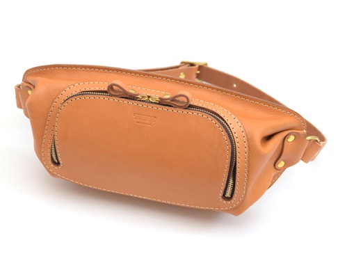 淺棕色皮革製成的斜背包，設有兩個拉鍊開口、一個頂部拉鍊和一個品牌標誌。包包上有縫線細節和黃銅色五金配件，包括可調節的肩帶。