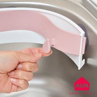 粉色塑膠製的開合式流理台廚餘架，邊緣為白色，一側配有紫色吸盤固定，手正操作其鎖扣。