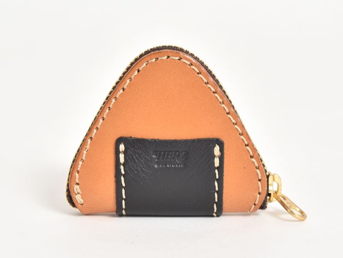 職人手作皮革零錢包，設計成三角飯糰造型，主體為淺棕色皮革，前方有一塊黑色皮革裝飾，車縫線為米白色，搭配金色拉鍊。