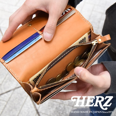 一只手打開一個棕褐色皮革長夾，露出內部的信用卡、日圓紙鈔和硬幣。