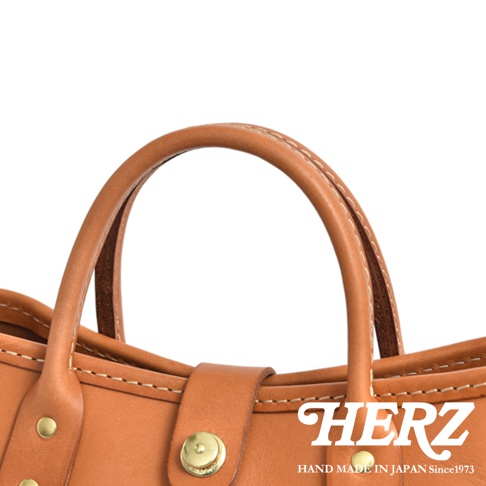 職人手作皮革迷你托特包 T-11，呈現溫潤的淺棕色皮革，搭配精緻縫線和黃銅色金屬扣件，展現簡約的設計風格。