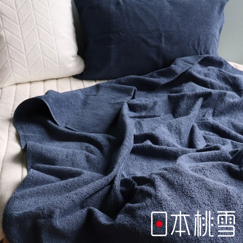 深藍色雙面毛圈棉毛巾被，柔軟舒適，鋪展在米白色床鋪上，搭配一個白色菱格紋枕頭和一個深藍色枕頭。