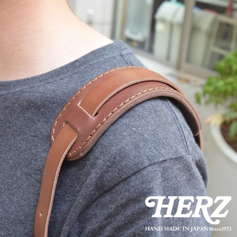 職人手作皮革肩墊，由兩層棕色皮革製成，縫線精緻，搭配灰色T恤，展現簡約質感。