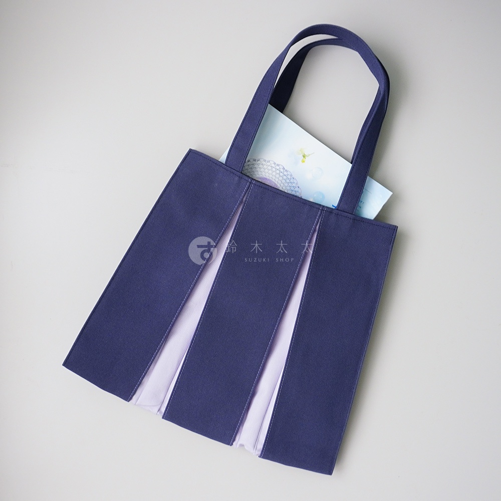 深藍色棉帆布扇形托特包，包身有三層扇形褶皺設計，內層為淺紫色帆布，配有兩條深藍色提把。