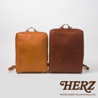 兩個職人手作皮革軟皮商務後背包，一個為淺棕色，另一個為深棕色。兩款背包皆為方形簡約設計，採用光滑皮革材質，並配有頂部提把及肩帶。