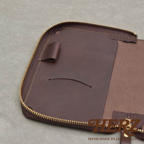 打開狀態的深棕色皮革記事本收納包，露出內部結構，有筆插和卡槽，拉鍊為金色。