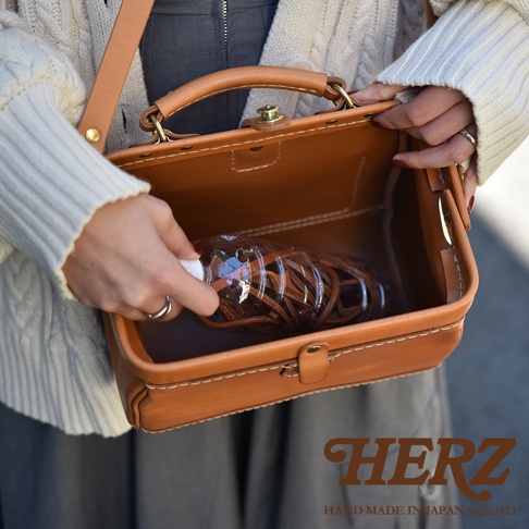 職人手作淺棕色皮革口金醫生單肩包，包身線條硬挺，配有可提握的提把，側面展示包內裝有水瓶，皮革材質質感佳，縫線工整。