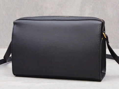 黑色皮革極簡風拉鍊單肩包，附有金色拉鍊和肩帶扣環，側面有精緻縫線。