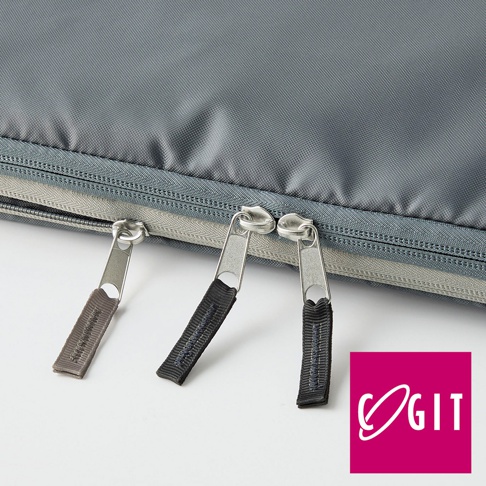 灰色織物表面，靠近底部有兩條並排的拉鍊，其中一條拉鍊的拉頭有灰色織帶，另一條拉鍊的拉頭有黑色織帶，織帶上印有細小的文字。右下角為粉紅色方形標誌，內有白色環形與字母「OGIT」。