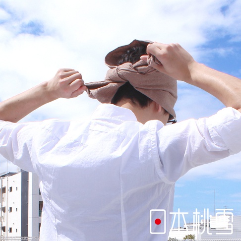 一名男子正在綁著淺棕色運動頭巾，頭巾材質看起來是柔軟的布料。他穿著白色長袖襯衫，背景是藍天白雲。