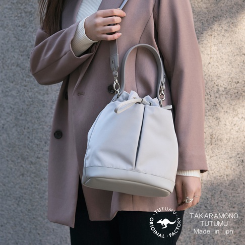 TAK​​ARAMONO TUTUMU Made in JPN，一位女士身穿粉色外套，手提灰色抽繩水桶包