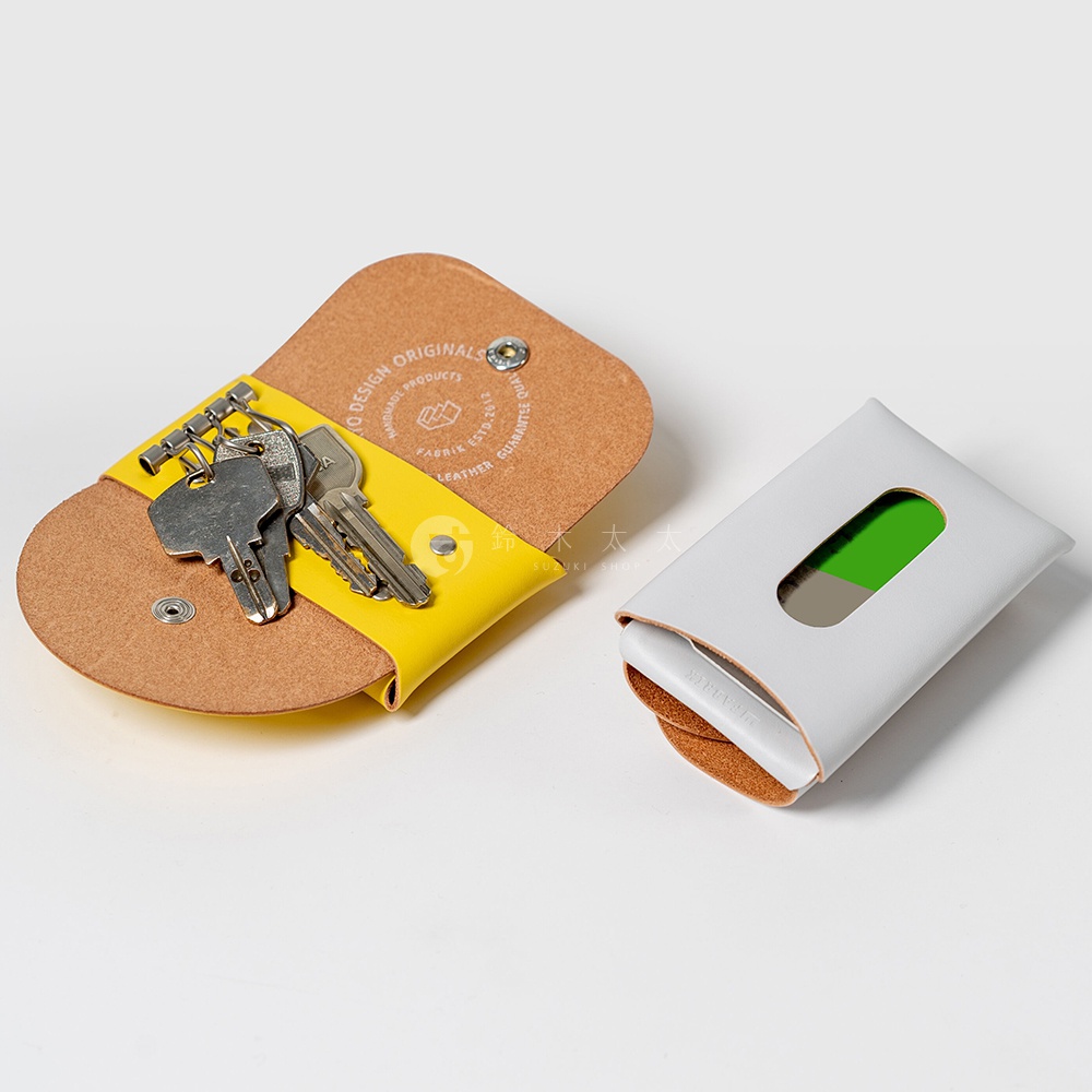 黃色和棕色皮革鑰匙包，內有銀色鑰匙，旁邊有一個白色和棕色的卡片套，其中綠色部分露出。