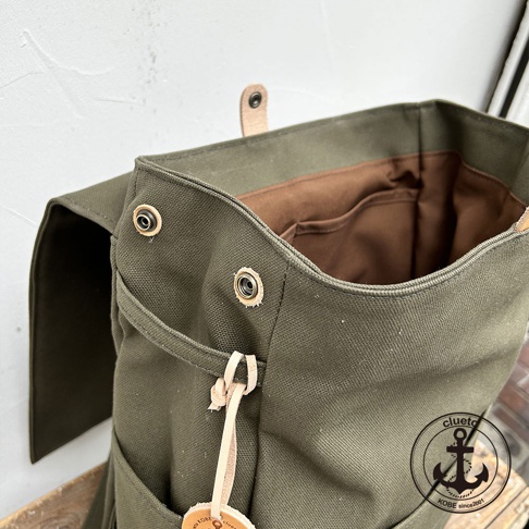 loiter 高島帆布前蓋式背包，綠色帆布材質，內有棕色內裡與多個隔層，外部有金屬卯扣及皮革束帶設計。