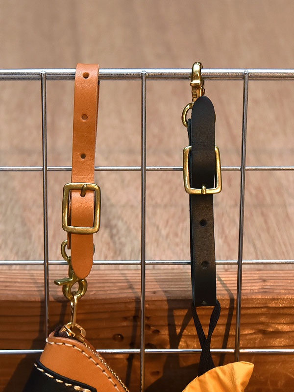 兩條職人手作皮革可調式吊掛帶，一條為淺棕色，另一條為黑色，皆配有黃銅色金屬扣環、鉤扣和調節器，懸掛於金屬網格上。